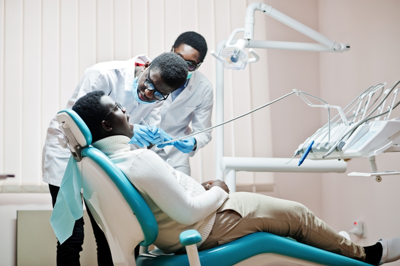 African american man patient in dental chair. Dentist office and doctor practice concept. Professional dentist helping his patient at dentistry medical. Drilling patient's teeth in clinic.